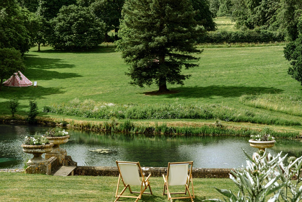 Luxurious contemporary hotel nestled in verdant Cotswolds countryside, featuring modern architecture and lush green landscape with historic manor house backdrop