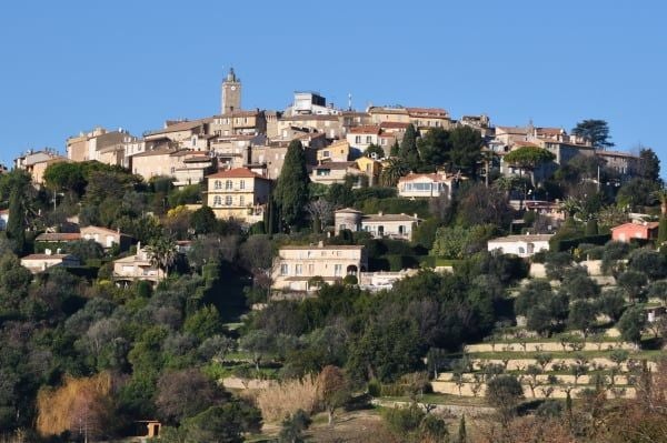 Elegant French boutique hotel with pale stone facade, lush rose gardens, and wrought-iron balconies nestled in a picturesque countryside landscape at golden hour