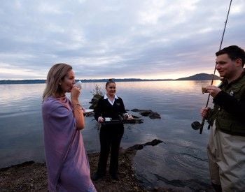 Luxurious lakeside hotel at sunset with glass walls reflecting alpine scenery, nestled on a scenic peninsula with dramatic mountain and water views in scenset.