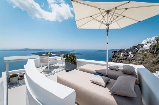 Whitewashed luxury cave hotel perched on Santorini's cliffside, featuring elegant blue-domed architecture and panoramic Aegean Sea views at sunset