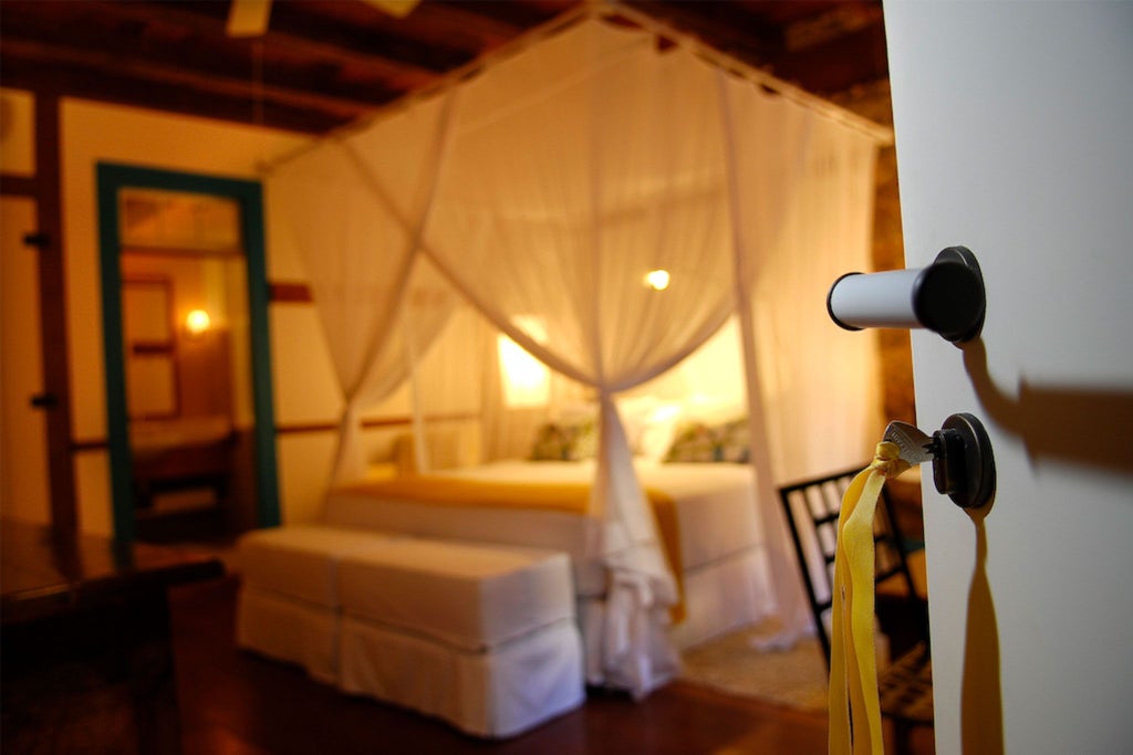 Luxurious yellow-themed suite at Casa Turquesa, featuring elegant Brazilian decor, plush white bedding, and warm afternoon sunlight casting golden hues