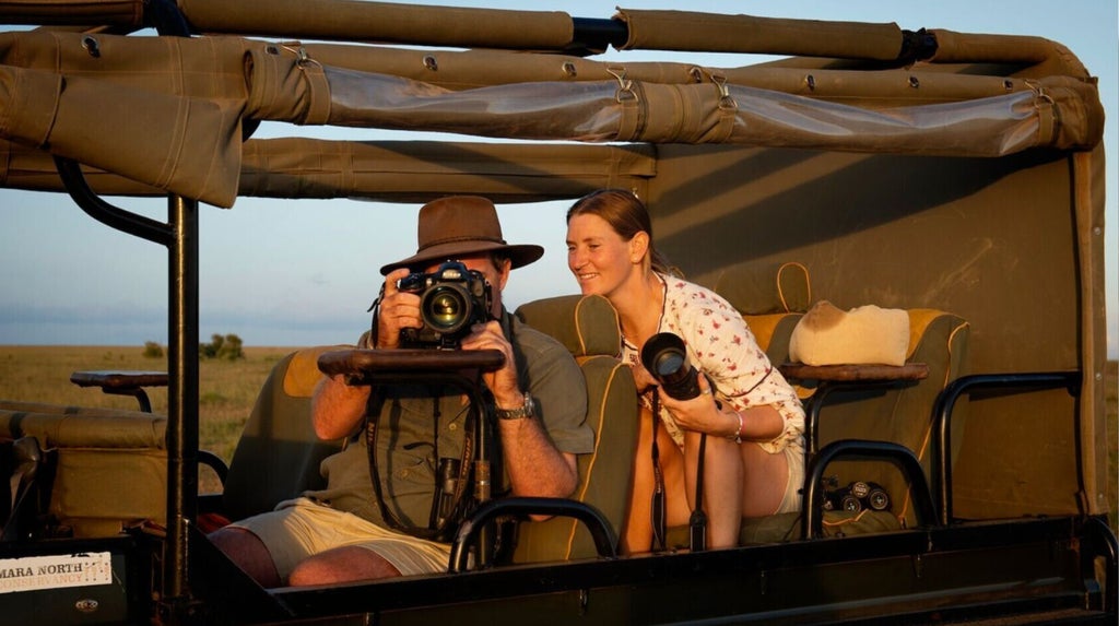 Luxurious safari tent with canopied bed overlooks vast Mara plains, featuring elegant furnishings and natural wood accents at dusk