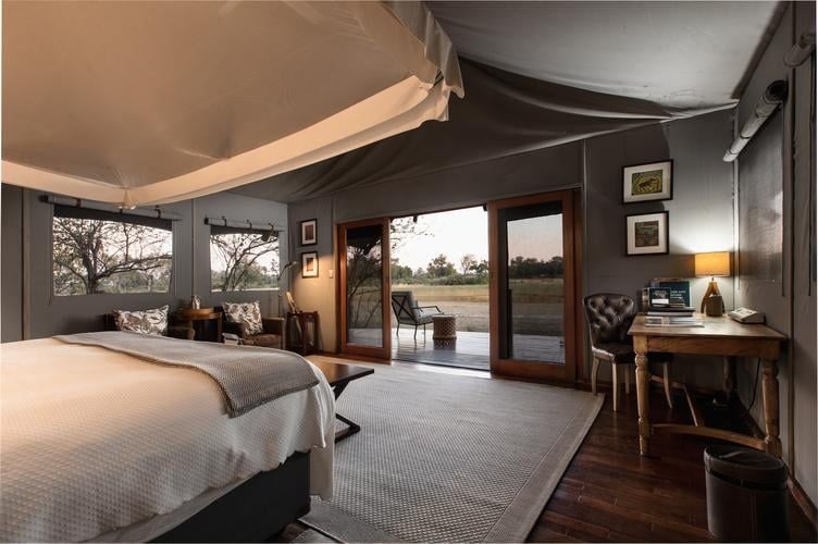 Luxurious safari-style tent-lodge bedroom with wooden floors, crisp white linens, and expansive views of Botswana's wilderness landscape at Chitabe Lediba Camp