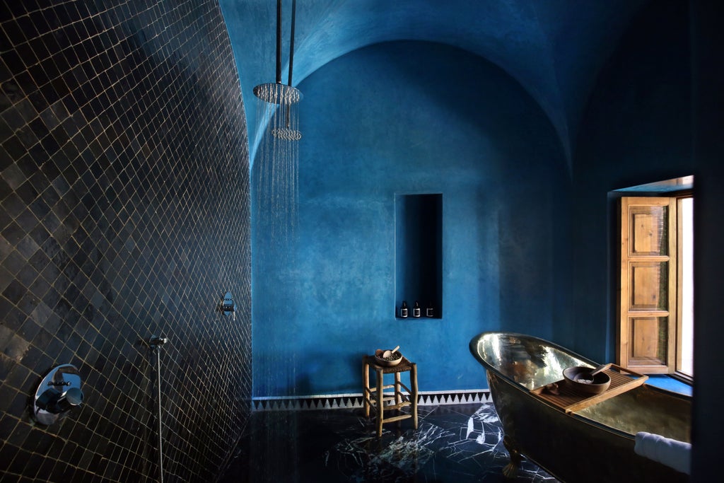 Luxurious Moroccan riad courtyard with emerald pool, pink walls, traditional archways and lush potted plants under blue skies