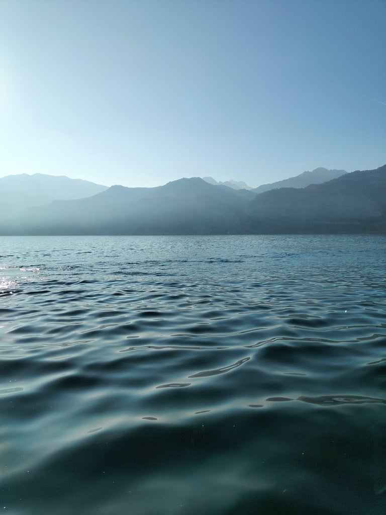 Mountains surround the tranquil waters of Lake Garda, with a luxury sailboat gliding past colorful Italian villas perched on rocky cliffs