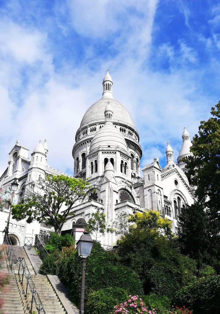 Cobblestone streets of Montmartre, Paris, with Sacré-Cœur Basilica in background, sunlight casting warm glow on charming Parisian architecture and cafe scene