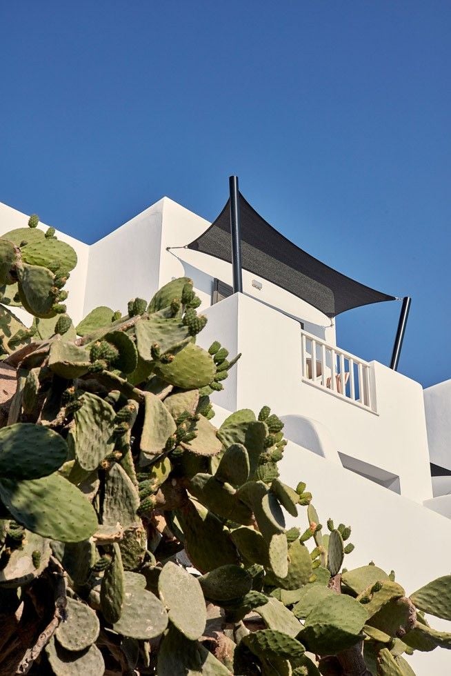 Whitewashed luxury hotel balconies with infinity pools overlooking Aegean Sea at sunset, nestled in Cycladic hillside architecture