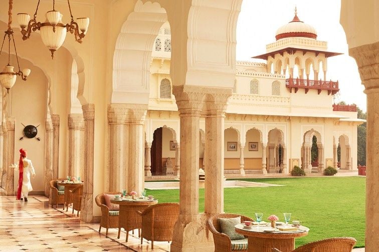 Ornate Rambagh Palace exterior with manicured gardens, grand archways and domed towers reflecting traditional Rajasthani architecture