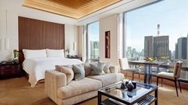 Modern, minimalist Premier Room at The Peninsula Tokyo with city skyline view, elegant neutral color palette, sleek contemporary furnishings, and large floor-to-ceiling windows showcasing urban landscape