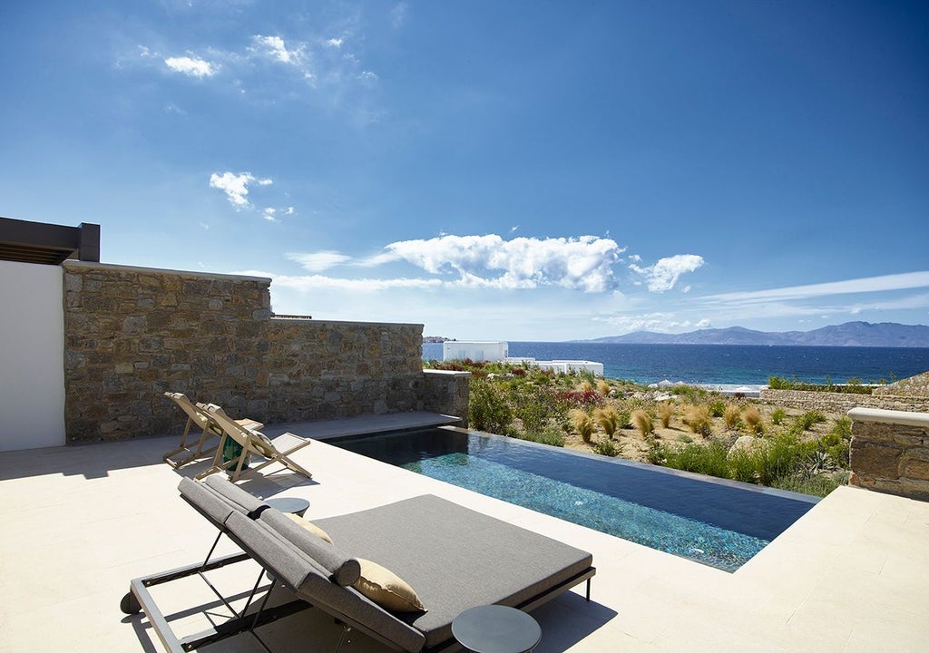 Luxurious one-bedroom suite with private heated pool overlooking azure Aegean Sea, featuring modern minimalist design and sweeping Mykonos coastline views