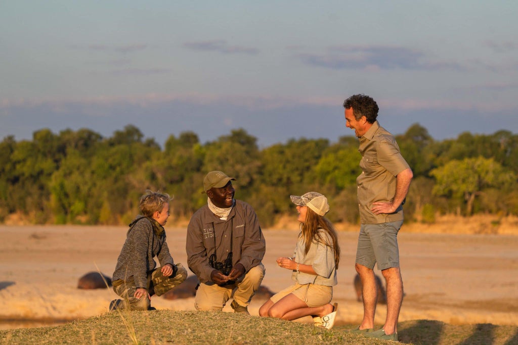 Luxurious canvas safari tent nestled in lush Zambian wilderness, overlooking golden grasslands of South Luangwa National Park at golden hour