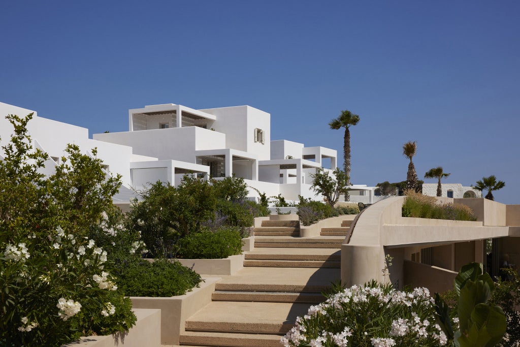 Elegant white-walled luxury hotel with curved architecture overlooking turquoise Mediterranean Sea, surrounded by flowering bougainvillea