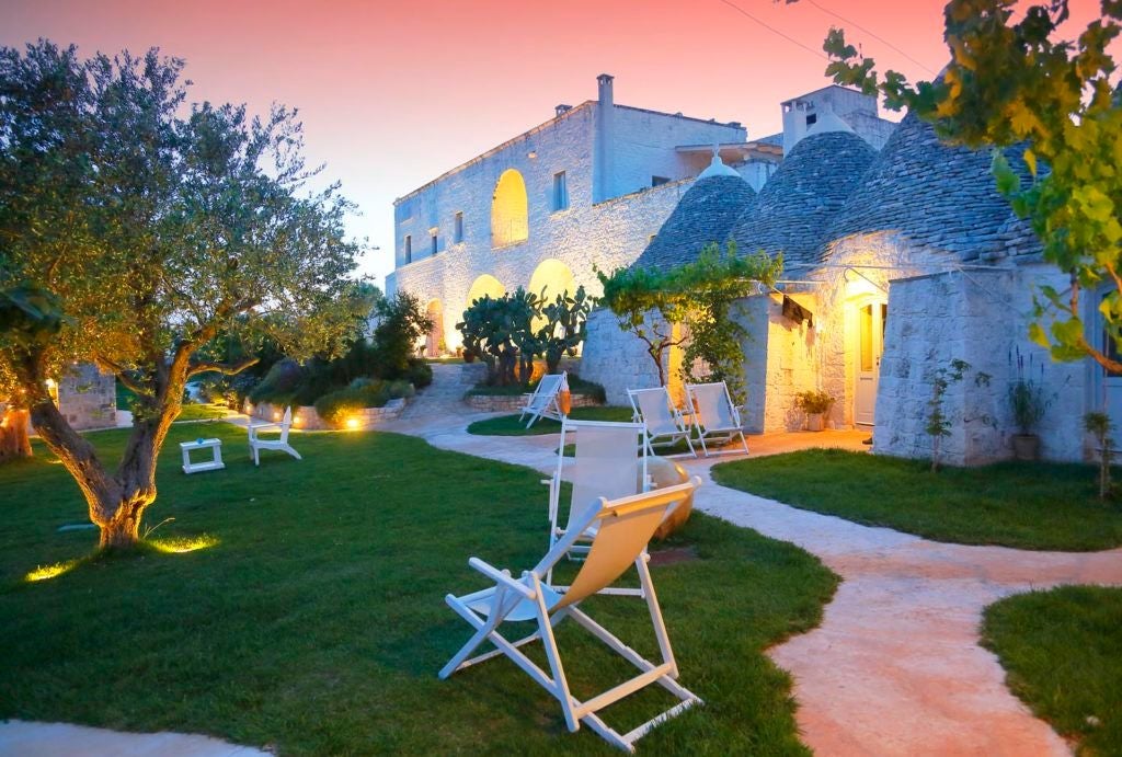 Rustic luxury stone farmhouse in Puglia, Italy, with whitewashed walls, traditional architecture, and lush olive grove surrounding serene country estate