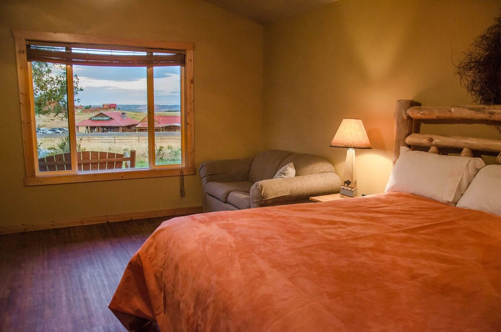 Rustic wooden cabin interior with plush king bed, large windows overlooking scenic mountain landscape at Zion Mountain Ranch in United States