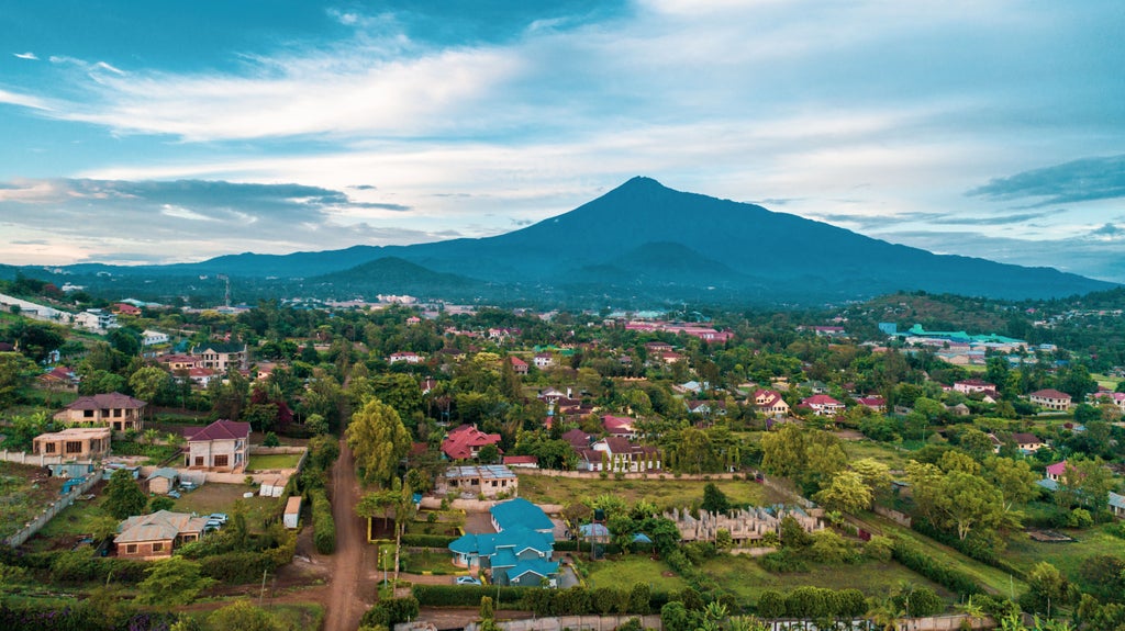 Alt: Aerial view of Arusha National Park in Tanzania, showing lush green plains with scattered acacia trees against Mount Meru's backdrop