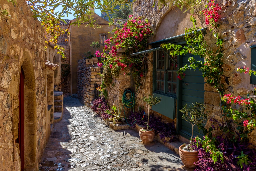 Medieval stone fortress of Monemvasia perched on rocky island cliff, azure Aegean waters below, golden sunlight illuminating historic Byzantine architecture and winding stone pathways