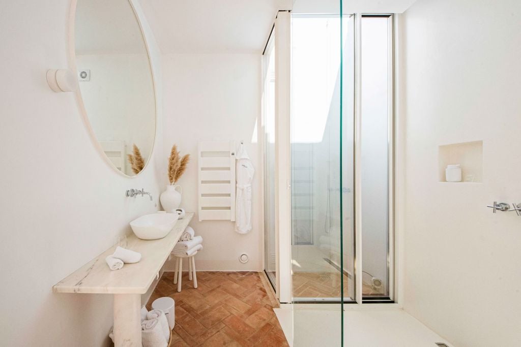 Modern Mediterranean-style hotel room with crisp white walls, natural wood furnishings, arched window, and organic textiles in soft earth tones