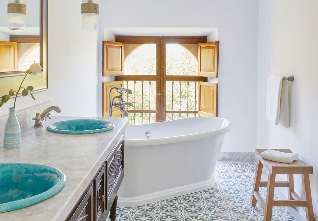 Elegant Mediterranean junior suite with terrace views, featuring a draped king bed, rustic wood beams, and traditional stone walls