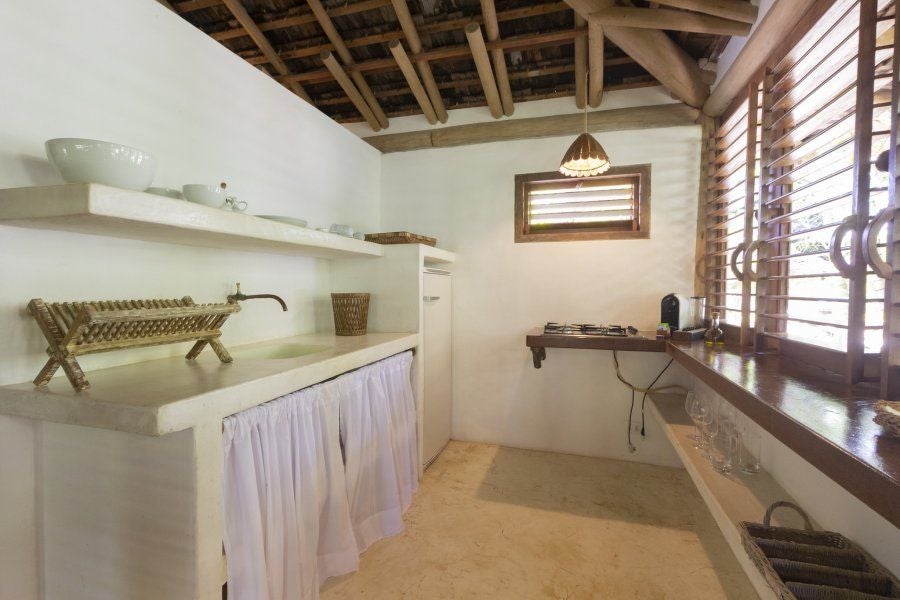 Rustic wooden furniture, white linens, and lush tropical greenery frame a serene bedroom at UXUA Casa Hotel and Spa in Trancoso, Brazil