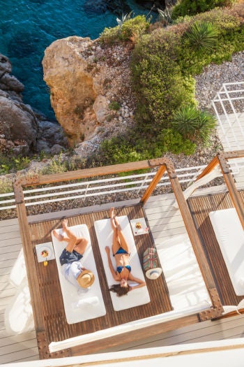 White luxury hotel built into rocky cliffs overlooking crystal-clear Adriatic Sea, with private beach deck and infinity pool in Dubrovnik