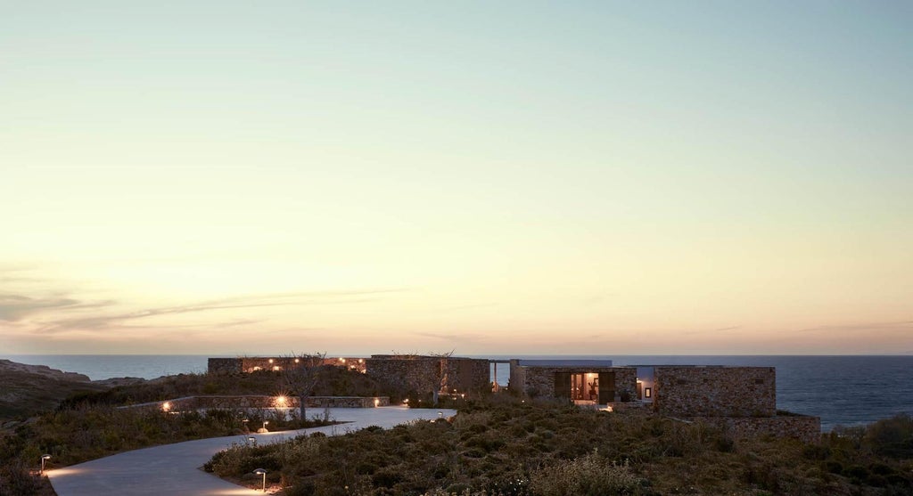 Minimalist Greek luxury resort nestled in hills, featuring stone architecture, infinity pool and panoramic Aegean Sea views at sunset