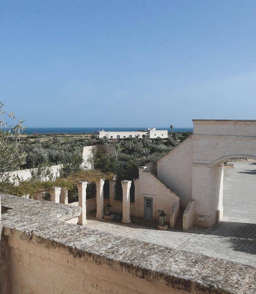 Elegant Mediterranean-style hotel room with soaring stone arch, cream furnishings, woven rug and ambient lantern lighting in Puglia