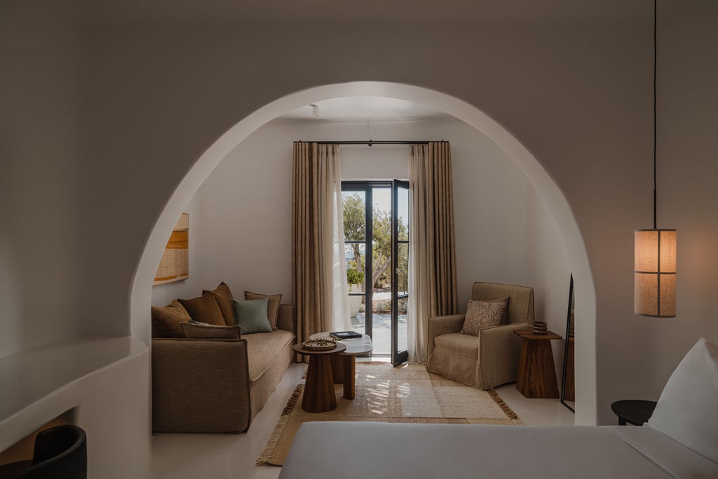 Minimalist luxury suite with infinity pool overlooking Santorini's caldera, featuring white curved architecture and sea views at sunset