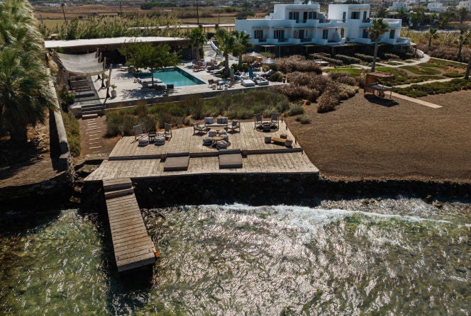 Luxurious coastal hotel SeeSoo in Santorini with white-washed buildings cascading down cliffs, featuring infinity pools overlooking the Aegean Sea