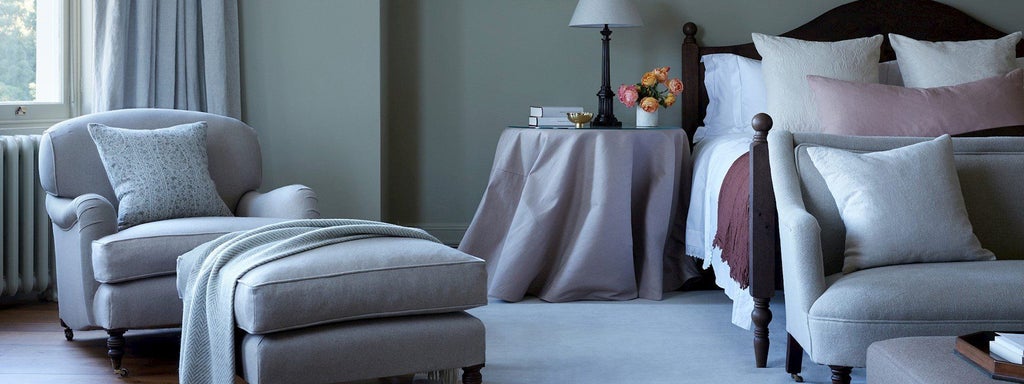 Luxurious neutral-toned bedroom with soft linens, elegant wood furnishings, and large windows overlooking verdant countryside at Heckfield Place hotel in UK