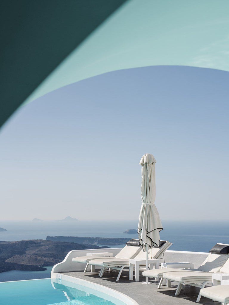 Luxurious white-washed Cycladic hotel overlooking azure Aegean waters, with elegant infinity pool and dramatic cliffside architecture in Santorini, Greece