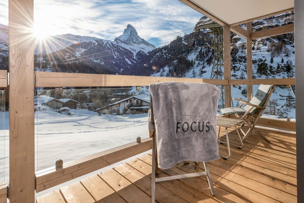 Modern luxury hotel with floor-to-ceiling windows reflecting snow-capped Matterhorn mountain, set against clear blue Alpine sky