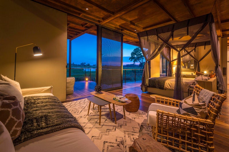 Elevated safari lodge with thatched roof and modern deck overlooking a pristine lagoon in Okavango Delta's untamed wilderness