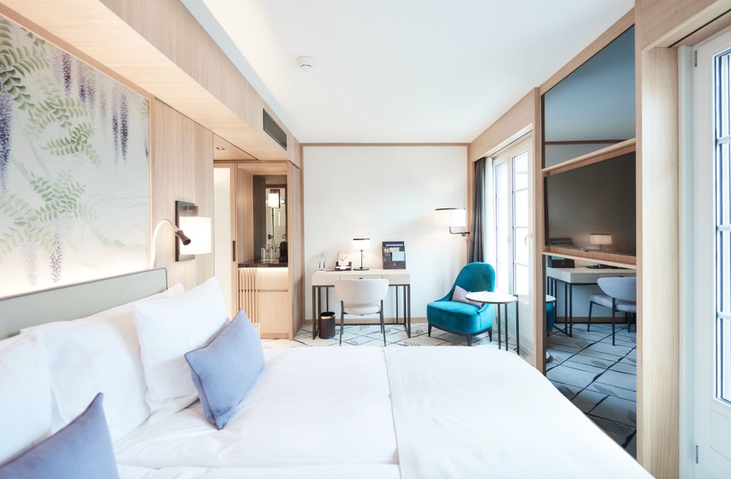 Modern hotel room with panoramic city views, private balcony, elegant furnishings, and king bed facing floor-to-ceiling windows in Zurich