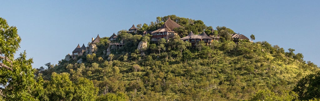 Luxurious safari lodge perched on rocky cliffside with panoramic savanna views, featuring infinity pool and open-air terrace design