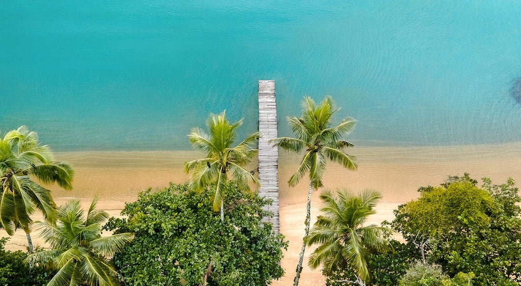 Elegant beachfront villa with infinity pool overlooking emerald bay, surrounded by lush Brazilian rainforest and private sandy cove