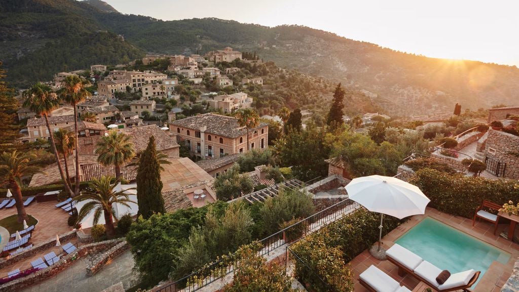 Elegant Mediterranean hotel facade with stone archways and ivy, surrounded by lush gardens against dramatic Tramuntana mountains