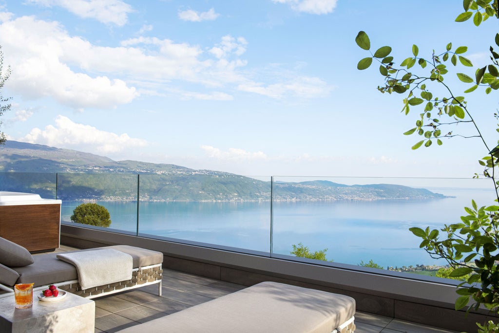 Modern luxury resort with infinity pool overlooking Lake Garda, featuring stone terraces and panoramic mountain views at sunset