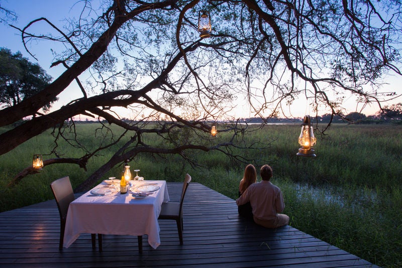 Elevated luxury safari lodge overlooking a watering hole with sun-drenched wooden deck, cushioned loungers, and a private plunge pool