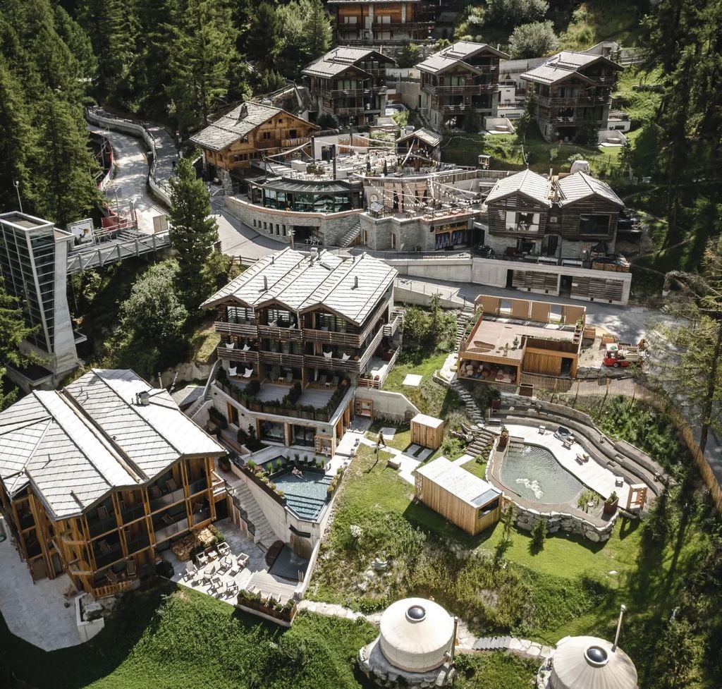 Luxurious wooden chalet-style resort nestled in snowy Swiss Alps, featuring modern glass facades and warm glowing balconies at dusk