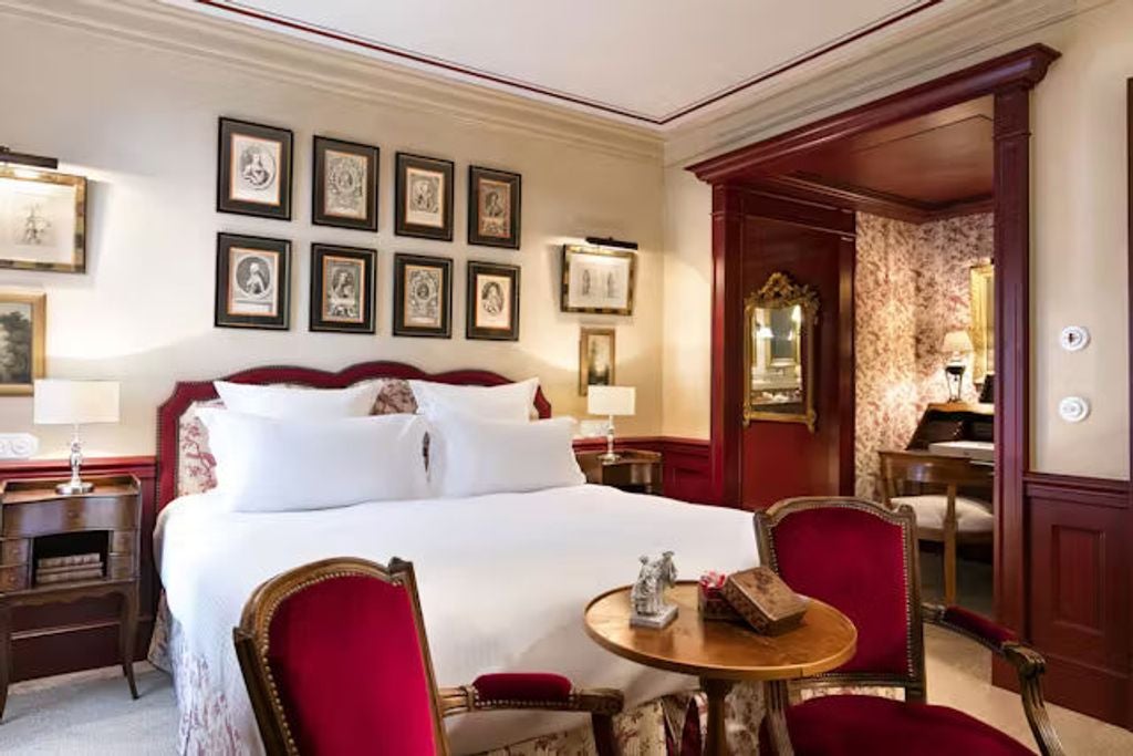 Elegant French hotel room with stone walls, ornate chandelier, vintage-style furnishings, and panoramic windows overlooking village views.