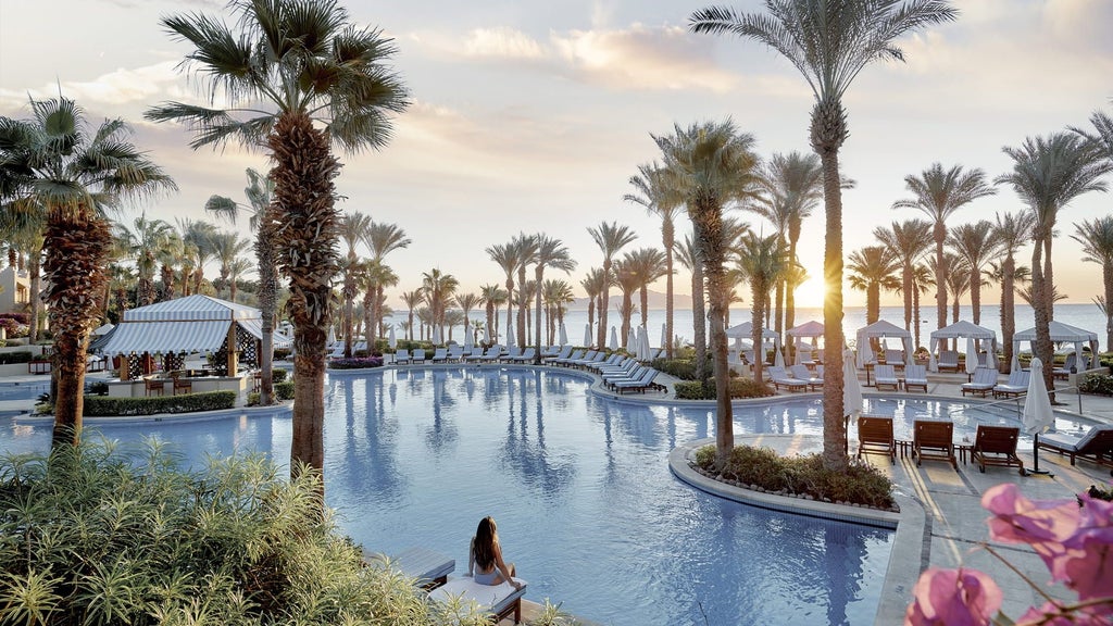 Luxury beachfront resort with white Arabian-style buildings cascading down cliffs overlooking the turquoise Red Sea and palm gardens