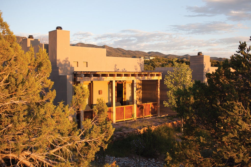 Adobe-style luxury resort with terra cotta walls, wooden beams, and desert landscaping set against backdrop of New Mexico mountains