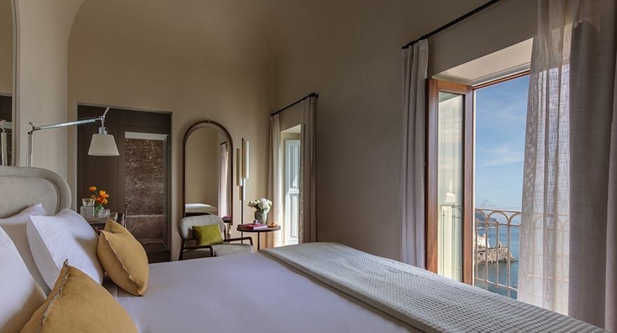 Elegant Mediterranean hotel room with arched windows, plush king bed, and sweeping Amalfi Coast views from a restored 13th-century convent