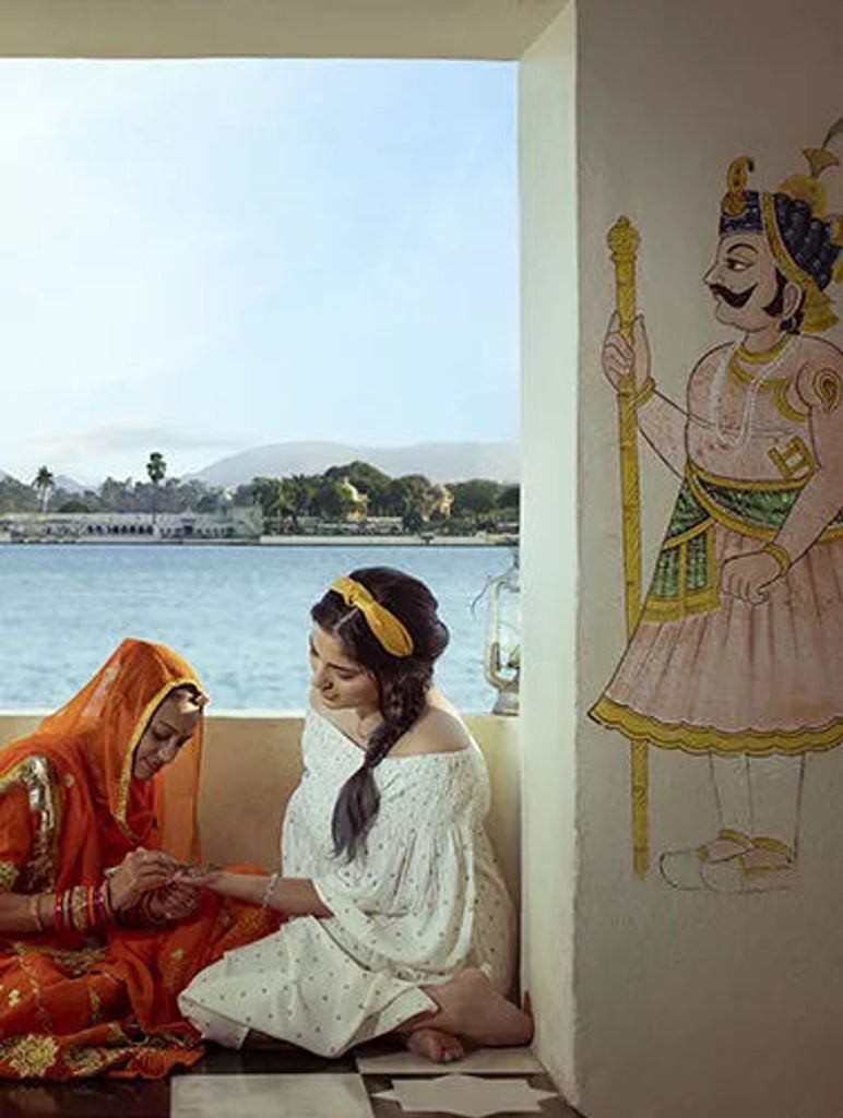 Opulent white marble palace hotel overlooking Lake Pichola, with ornate domes, archways and manicured gardens at sunset in Udaipur