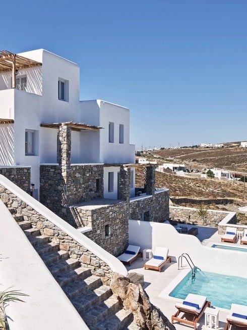 Pristine white luxury villa overlooking azure Aegean Sea, cascading infinity pools against dramatic Santorini cliffside at golden sunset hour