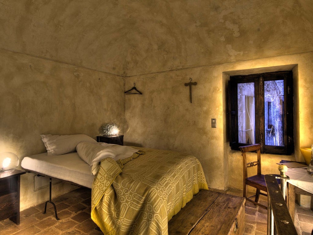 Rustic Italian hotel room with stone walls, antique wooden furnishings, and a panoramic view of a historic bell tower through a softly draped window