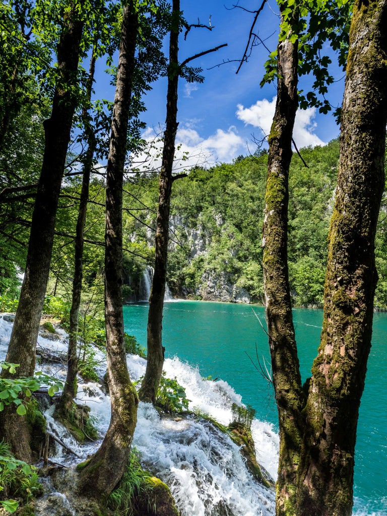 Turquoise waterfalls cascade between wooden boardwalks at Plitvice Lakes National Park, with lush forest and crystal-clear pools below