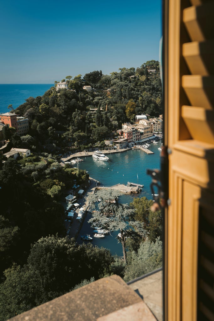 Luxury wooden boat cruising along Portofino's crystal-clear waters, passing colorful historic mansions and exclusive harborfront villas