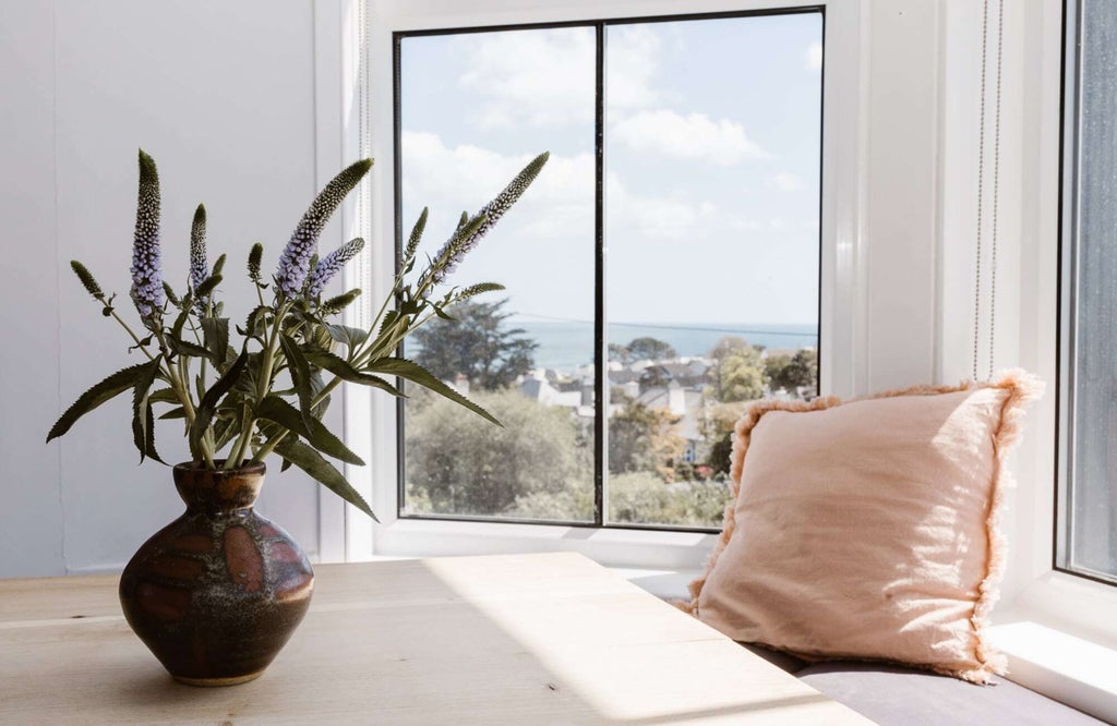 Luxurious bedroom with crisp white linens, plush throw pillows, elegant wooden furniture, and soft natural light highlighting coastal-inspired decor in UK hotel room