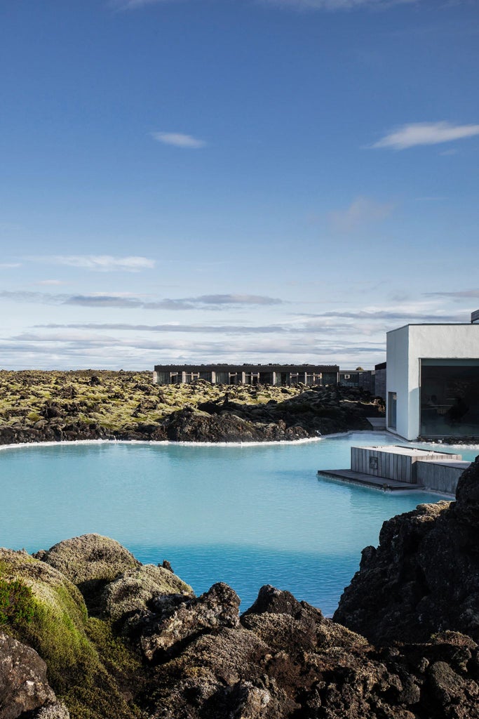 Minimalist Icelandic luxury hotel room with blue-gray volcanic stone walls, crisp white linens, and panoramic landscape window view